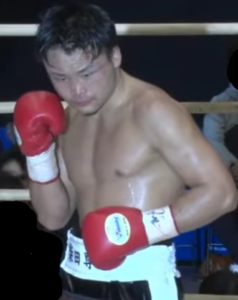 プロボクサー柴田尊文選手がリング上で構える姿。赤いグローブを着用し、集中した表情で前方を見つめている。